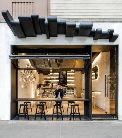 La façade vitrée de Maison Kafé, avec ses tabourets en terrasse et son auvent noir.